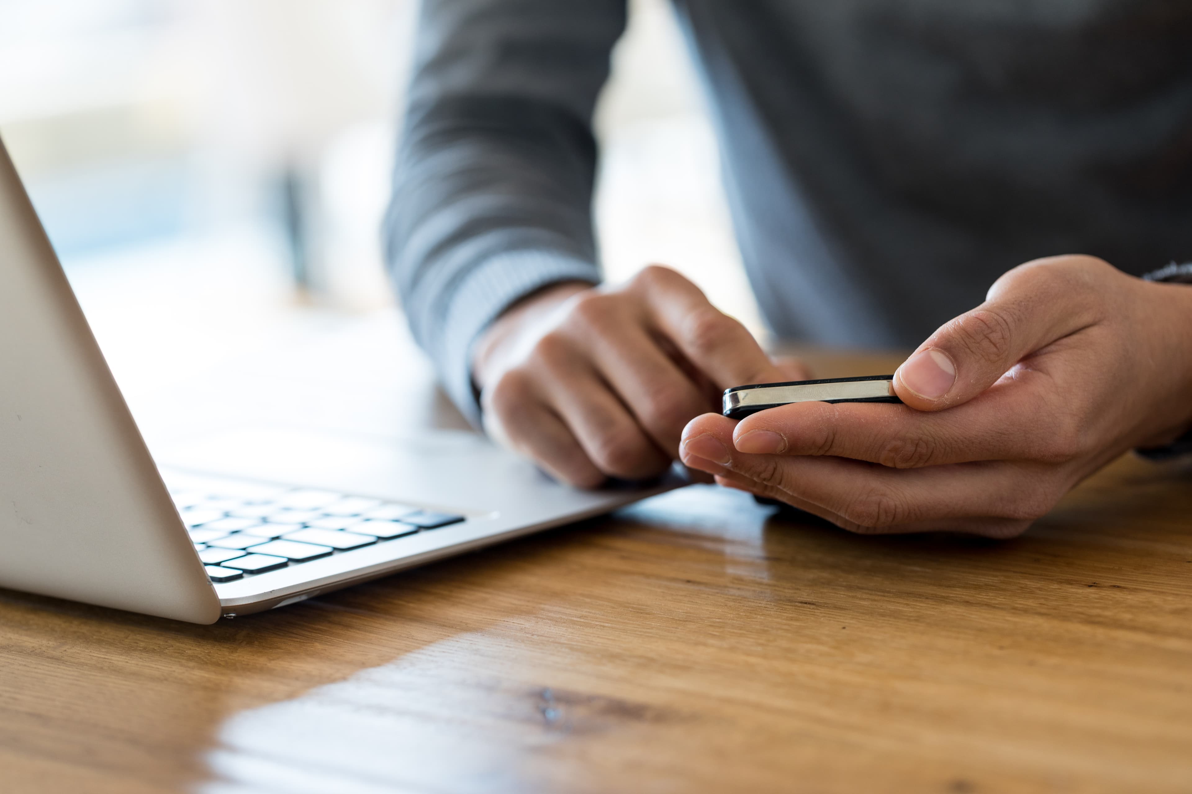 a person using a phone and a laptop on a desk